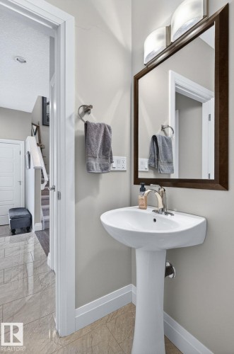 Pedestal sink with polished chrome faucet, framed mirror, wall-mounted light fixture, and tile flooring - 83 Sandalwood Place, Leduc, AB - Indoor Photo Showing Bathroom