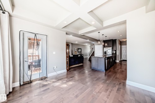 Spacious open-concept interior featuring wood-finish flooring, a kitchen island with pendant lighting, and a glass-paneled exterior door - 4155 Charles Link, Edmonton, AB - Indoor Photo Showing Other Room