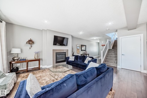 Spacious living area featuring a fireplace with tile surround, recessed lighting, wood-finish flooring, and a carpeted staircase with white railings - 4155 Charles Link, Edmonton, AB - Indoor Photo Showing Living Room With Fireplace