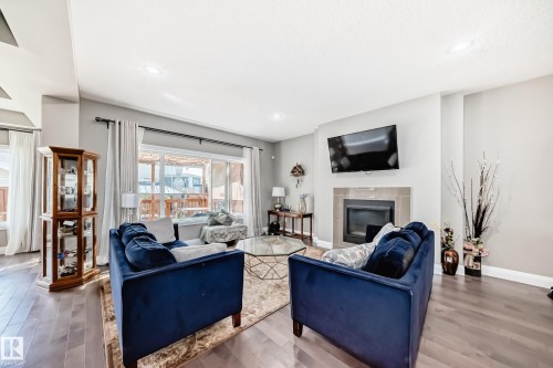 Living area featuring wood-finish flooring, a contemporary fireplace with a tile surround, recessed lighting, and large sliding glass doors leading to an exterior space - 4155 Charles Link, Edmonton, AB - Indoor Photo Showing Living Room With Fireplace