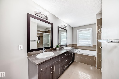 Bathroom featuring a dual vanity with dark wood-finish cabinetry, a built-in tub with tile surround, a large framed mirror, and tile flooring - 4155 Charles Link, Edmonton, AB - Indoor Photo Showing Bathroom
