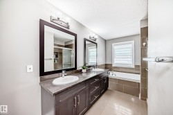 Bathroom featuring a dual vanity with dark wood-finish cabinetry, a built-in tub with tile surround, a large framed mirror, and tile flooring - 