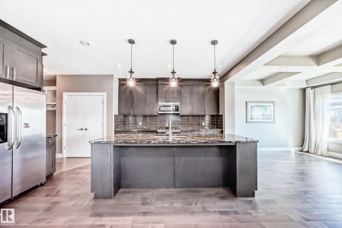 Modern kitchen featuring a large central island with a stone countertop, dark wood-finish cabinetry, stainless steel appliances, and pendant lighting - 4155 Charles Link, Edmonton, AB - Indoor Photo Showing Kitchen With Upgraded Kitchen