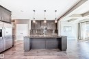 Modern kitchen featuring a large central island with a stone countertop, dark wood-finish cabinetry, stainless steel appliances, and pendant lighting - 4155 Charles Link, Edmonton, AB  - Indoor Photo Showing Kitchen With Upgraded Kitchen 