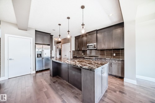 Kitchen featuring a large central island with a stone countertop, coordinating dark cabinetry, stainless steel appliances, and wood-finish flooring - 4155 Charles Link, Edmonton, AB - Indoor Photo Showing Kitchen With Upgraded Kitchen