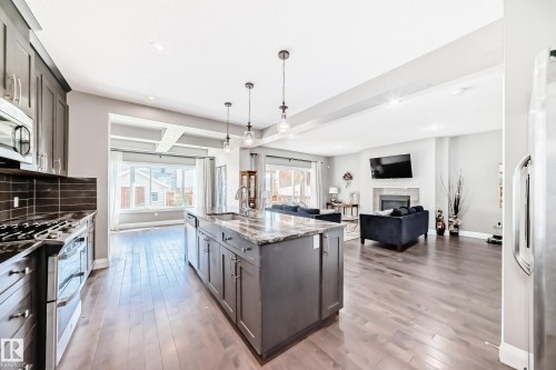 Open-concept kitchen featuring an island with a sink and pendant lighting, dark wood-finish flooring, stainless steel appliances, and dark cabinetry - 4155 Charles Link, Edmonton, AB - Indoor Photo Showing Kitchen With Upgraded Kitchen