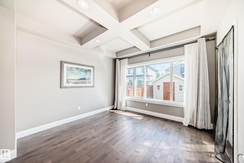 Spacious room featuring wood-finish flooring, a coffered ceiling with recessed lighting, and a large picture window - 4155 Charles Link, Edmonton, AB - Indoor Photo Showing Other Room