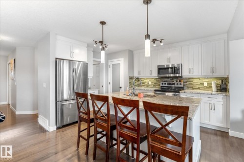 Kitchen featuring white cabinetry, stainless steel appliances, a multi-tone tile backsplash, and an island with a stone countertop - 3 Richmond Link, Fort Saskatchewan, AB - Indoor