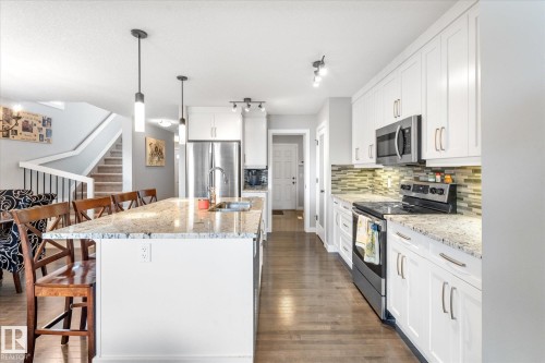 Bright kitchen featuring white shaker cabinetry, stainless steel appliances, a multi-tone tile backsplash, and wood-finish flooring - 3 Richmond Link, Fort Saskatchewan, AB - Indoor Photo Showing Kitchen With Upgraded Kitchen