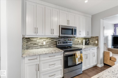 Bright kitchen featuring white shaker cabinetry, stainless steel appliances, granite countertops, glass tile backsplash, and under-cabinet lighting - 3 Richmond Link, Fort Saskatchewan, AB - Indoor Photo Showing Kitchen