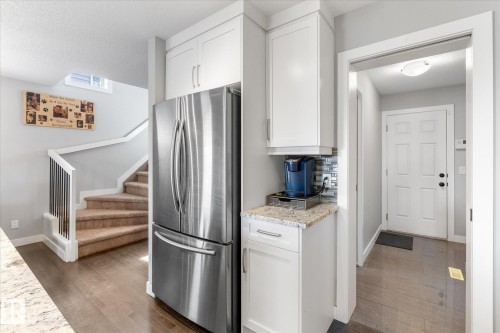 Stainless steel refrigerator flanked by white shaker-style cabinetry with a granite-look countertop and mosaic tile backsplash - 3 Richmond Link, Fort Saskatchewan, AB - Indoor