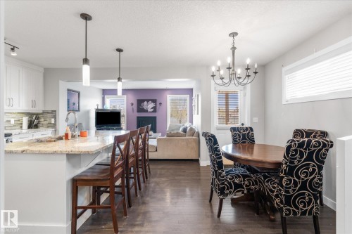Open-concept living area featuring a kitchen island with seating, dark wood-finish flooring, white cabinetry, and a dining area with a chandelier - 3 Richmond Link, Fort Saskatchewan, AB - Indoor Photo Showing Dining Room