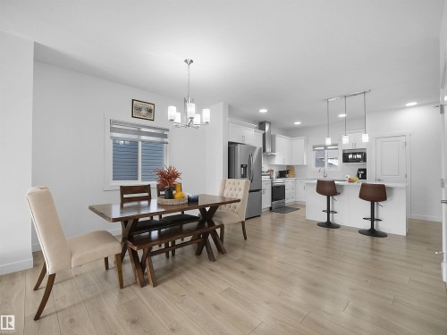Open-concept kitchen and dining area featuring light wood-finish flooring, white cabinetry, stainless steel appliances, a kitchen island with pendant lighting, and a chandelier over the dining space - 30 Hope Cm, Spruce Grove, AB - Indoor Photo Showing Dining Room