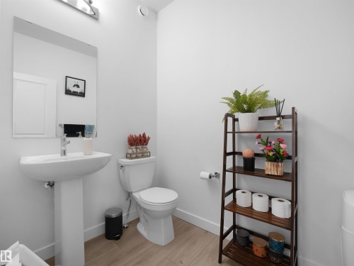 Pedestal sink with chrome faucet, large rectangular wall mirror, wood-finish flooring, and white walls - 30 Hope Cm, Spruce Grove, AB - Indoor Photo Showing Bathroom