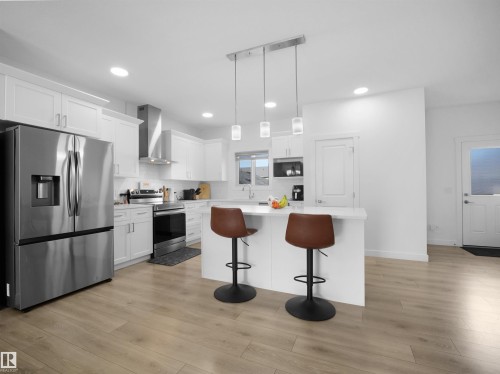 Kitchen featuring white cabinetry, stainless steel appliances, a center island with pendant lighting, recessed ceiling lights, and wood-finish flooring - 30 Hope Cm, Spruce Grove, AB - Indoor Photo Showing Kitchen With Upgraded Kitchen