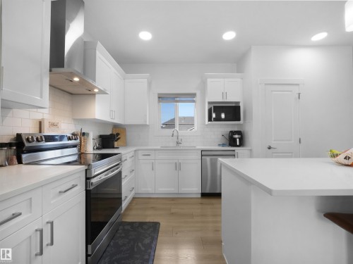Modern kitchen featuring white shaker cabinetry, stainless steel appliances, light countertops, and wood-finish flooring - 30 Hope Cm, Spruce Grove, AB - Indoor Photo Showing Kitchen With Upgraded Kitchen