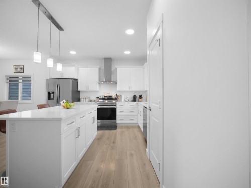 Contemporary kitchen featuring a large island with white cabinetry, stainless steel appliances, pendant lighting, and wood-finish flooring - 30 Hope Cm, Spruce Grove, AB - Indoor Photo Showing Kitchen With Upgraded Kitchen