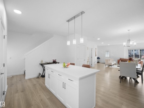 Open-concept living space featuring wood-finish flooring, a white kitchen island with a light-toned countertop and pendant lighting, and recessed ceiling lights - 30 Hope Cm, Spruce Grove, AB - Indoor