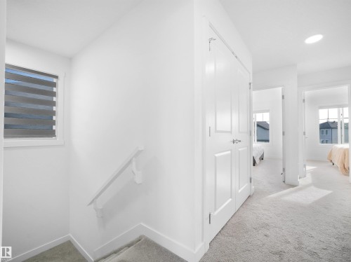 Upper-level hallway with white paneled doors, light grey carpet, and a large window featuring horizontal blinds - 30 Hope Cm, Spruce Grove, AB - Indoor Photo Showing Other Room
