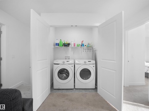 Dedicated laundry closet featuring a front-loading washer and dryer set, an overhead wire shelving unit, and a tiled floor - 30 Hope Cm, Spruce Grove, AB - Indoor Photo Showing Laundry Room