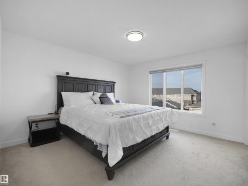 Bright bedroom featuring light-toned carpeting, white walls, and a large multi-pane window with a roller shade - 30 Hope Cm, Spruce Grove, AB - Indoor Photo Showing Bedroom
