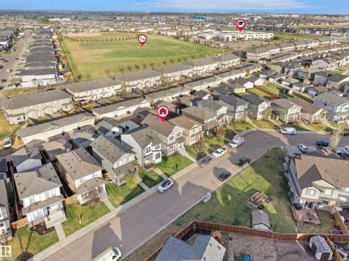 Aerial view of a residential neighborhood with detached homes, featuring street parking, a central green space, and visible community buildings - 30 Hope Cm, Spruce Grove, AB - Outdoor With View