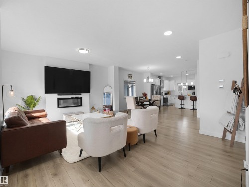 Open-concept living area featuring light wood-finish flooring, recessed lighting, and a contemporary wall-mounted electric fireplace - 30 Hope Cm, Spruce Grove, AB - Indoor Photo Showing Living Room