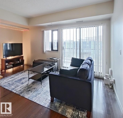 Living area featuring wood-finish flooring, a large sliding glass door to a private balcony, and an additional window - 707 10319 111 Street Nw, Edmonton, AB - Indoor Photo Showing Living Room