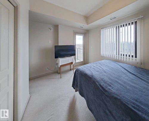 Carpeted room featuring a window with vertical blinds and a glass door providing outdoor access - 707 10319 111 Street Nw, Edmonton, AB - Indoor Photo Showing Bedroom