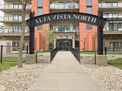 Building entrance featuring a prominent arched sign, stone facade elements, and a concrete pathway with black metal railings - 707 10319 111 Street Nw, Edmonton, AB - Outdoor With Balcony With Facade