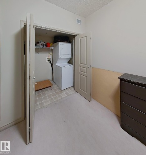 Dedicated laundry closet with stacked washer and dryer, tile flooring, and integrated shelving - 707 10319 111 Street Nw, Edmonton, AB - Indoor Photo Showing Laundry Room