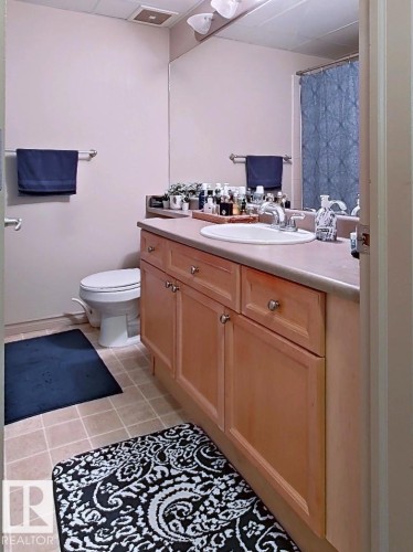 Bathroom featuring a light wood-finish vanity with a built-in sink and chrome faucet, a large wall-mounted mirror, and tile flooring - 707 10319 111 Street Nw, Edmonton, AB - Indoor Photo Showing Bathroom