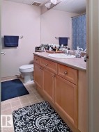 Bathroom featuring a light wood-finish vanity with a built-in sink and chrome faucet, a large wall-mounted mirror, and tile flooring - 