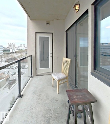 Outdoor balcony featuring concrete flooring, glass and metal railing, and a wall-mounted exterior light fixture - 707 10319 111 Street Nw, Edmonton, AB - Outdoor With Balcony With Exterior