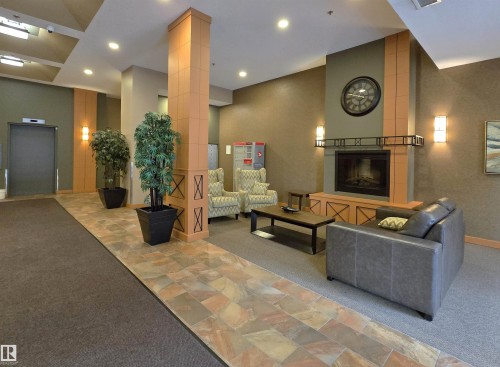 Lobby area featuring a modern fireplace with a decorative mantel, sconce lighting, and a stone-look tile pathway - 707 10319 111 Street Nw, Edmonton, AB - Indoor Photo Showing Other Room With Fireplace