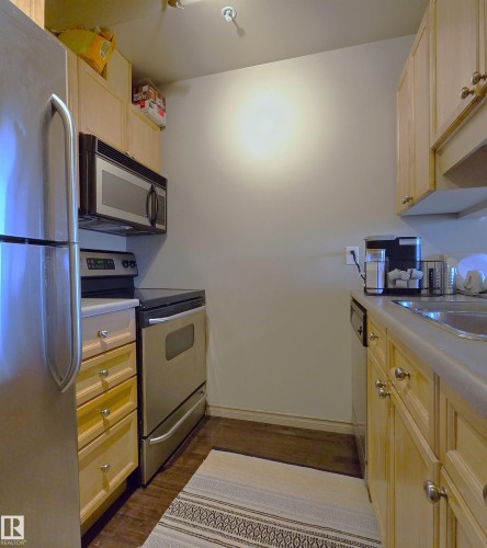 Compact kitchen featuring light wood cabinetry and stainless steel appliances, including a refrigerator, range, and microwave - 707 10319 111 Street Nw, Edmonton, AB - Indoor Photo Showing Kitchen