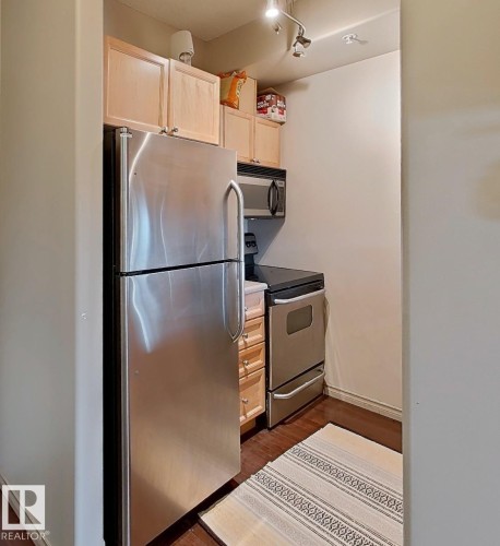 Compact kitchen featuring stainless steel appliances, light wood-finish cabinetry, dark wood-finish flooring, and track lighting - 707 10319 111 Street Nw, Edmonton, AB - Indoor Photo Showing Kitchen