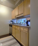 Kitchen featuring light wood cabinetry, a stainless steel dishwasher, a single basin sink with a chrome faucet, and light-toned countertops - 