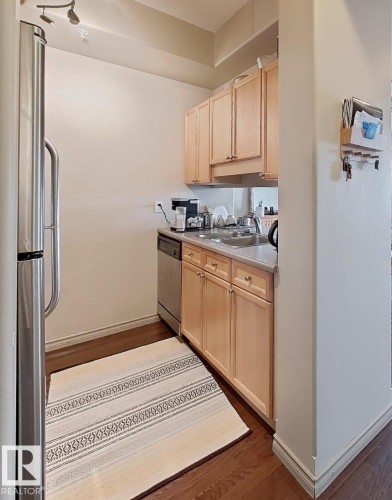 Compact kitchen featuring wood-finish flooring, light wood cabinetry, and a stainless steel refrigerator - 707 10319 111 Street Nw, Edmonton, AB - Indoor Photo Showing Kitchen With Double Sink