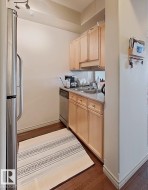 Compact kitchen featuring wood-finish flooring, light wood cabinetry, and a stainless steel refrigerator - 