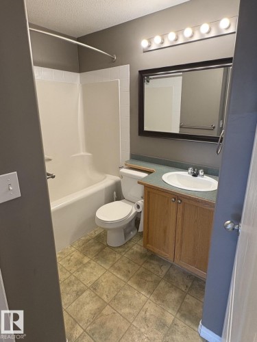 Bathroom featuring a wood-finish vanity with an integrated sink and green-toned countertop, a framed mirror, and a five-bulb vanity light fixture - 138 9525 162 Avenue, Edmonton, AB 