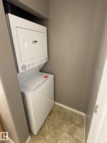 Dedicated laundry area featuring a stacked washer and dryer unit, neutral wall color, and tile flooring - 138 9525 162 Avenue, Edmonton, AB 