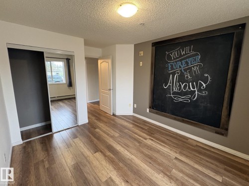 Interior room featuring wood-finish flooring, a large chalkboard accent wall with a dark wood frame, and a semi-flush ceiling light fixture - 138 9525 162 Avenue, Edmonton, AB 