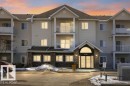 Multi-story residential building featuring light-colored siding, stone facade accents, multiple private balconies with white railings, and a prominent arched entryway - 138 9525 162 Avenue, Edmonton, AB 