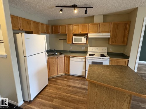 Kitchen featuring wood-finish cabinetry, a white appliance suite, a built-in microwave, and wood-finish flooring - 138 9525 162 Avenue, Edmonton, AB 