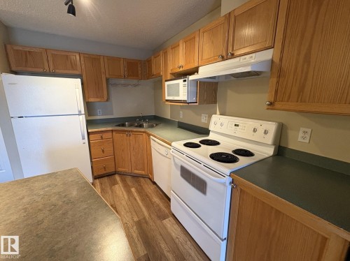 Kitchen featuring wood-finish cabinetry, green laminate countertops, and wood-finish flooring - 138 9525 162 Avenue, Edmonton, AB 