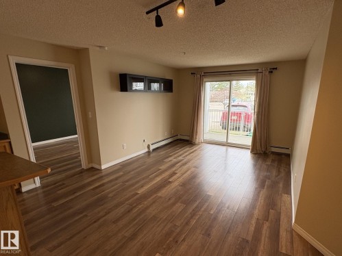 Spacious living area featuring wood-finish flooring, neutral wall tones, and a sliding glass door providing access to an outdoor space - 138 9525 162 Avenue, Edmonton, AB 