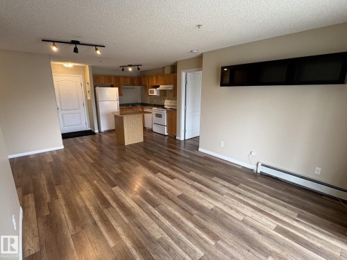 Expansive living area featuring wood-finish flooring, neutral wall tones, and a track lighting fixture - 138 9525 162 Avenue, Edmonton, AB 