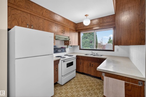Kitchen featuring wood cabinetry, white appliances, a double basin sink, light-toned countertops, and a window providing exterior views - 8407 150 Avenue, Edmonton, AB - Indoor Photo Showing Kitchen With Double Sink