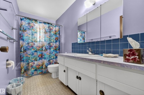 Bathroom featuring a single basin vanity with a laminate countertop, white cabinetry with dark hardware, a medicine cabinet, a full bathtub with shower, and patterned flooring - 8407 150 Avenue, Edmonton, AB - Indoor Photo Showing Bathroom